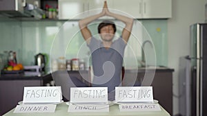 A young man meditates in frint of a table with empty plates on which writtings ` fasting` are placed. Yoga diet