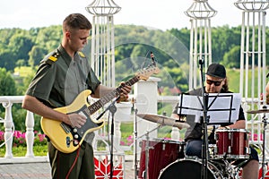 A young man in a military uniform with a guitar in his hands and a drummer at a concert. Open-air military concert in Moscow