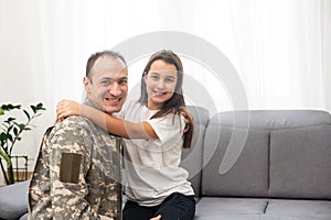 Young man in military uniform with his wife on sofa at home