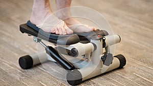 A young man on a mini stepper does a leg warm-up. Modern lifestyle, indoor sports.