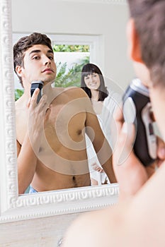 Young man in mirror shaving with electric shaver