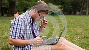 Young man with mobile and laptop phone sitting on a grass.