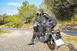 Young man with mobile phone on motorcycle in nature.