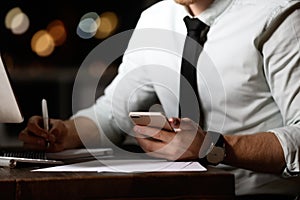 Young man with mobile phone working in office at night