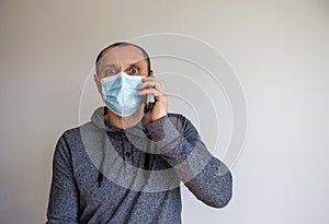 Young man with mobilphone wearing a protective medicine mask isolated on white background. COVID-19 pandemic concept. Copy space