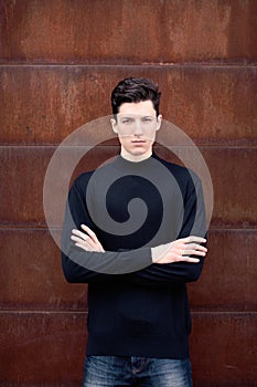 The young man model in a black jacket poses at a metal rusty wall