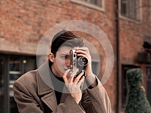 The young man model in a coat photographs the vintage camera