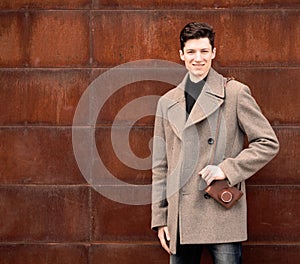 The young man model in a coat poses at a metal rusty wall with the vintage camera on a shoulder