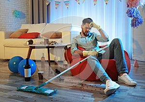 Young man with mop suffering from hangover in room after party