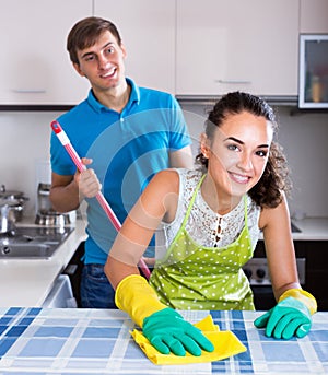Young man mopping and smiling woman dusting