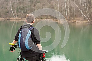 Young man on mountain bike relaxes, on background flooded mine