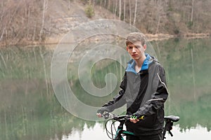 Young man on mountain bike relaxes, on background flooded mine