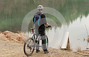 Young man on mountain bike relaxes, on background flooded mine