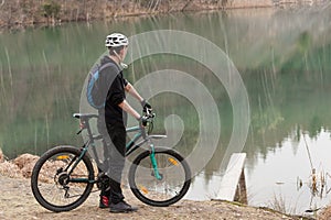 Young man on mountain bike relaxes, on background flooded mine