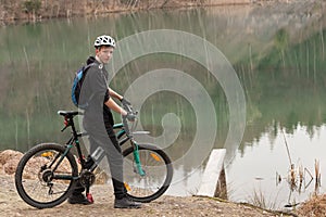 Young man on mountain bike relaxes, on background flooded mine
