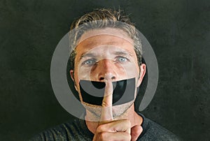 Young man with mouth and lips sealed covered with adhesive tape in censorship coerced freedom of speech and forced silence and sec