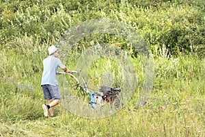 A young man mows hay with a motor in a field on a clear summer day