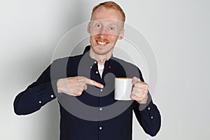 A young man with a mug of tea or coffee. He pleased. White background. Redhead male with white mug.