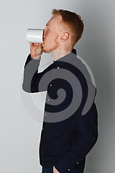 A young man with a mug of tea or coffee. He pleased. White background. Redhead male with white mug.