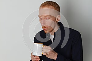 A young man with a mug of tea or coffee. He pleased. White background. Redhead male with white mug.