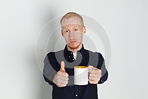 A young man with a mug of tea or coffee. He pleased. White background. Redhead male with white mug.