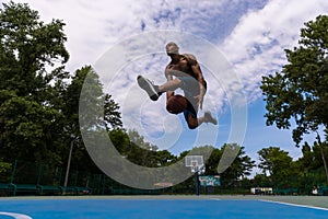 Young man, muscular african male basketball player playing basketball at street public stadium, sport court or