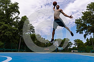 Young man, muscular african male basketball player playing basketball at street public stadium, sport court or
