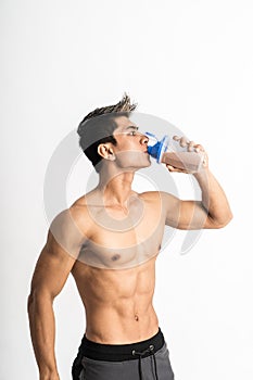 Young man with muscular body holding a bottle and drink with one hand stand facing side