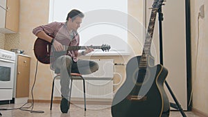 Young man musician composes music on the guitar and plays in the kitchen, other musical instrument in the foreground,