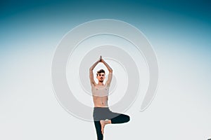 Young man in a Namaste greeting position while freeing his mind from worries in tree pose