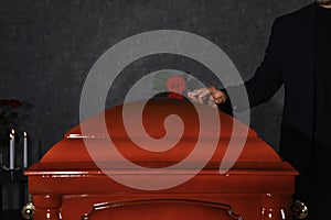 Young man near casket with red rose in funeral home,