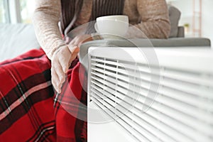Young man near electric heater at home. Concept of heating season photo