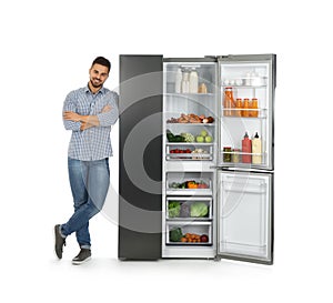 Young man near open refrigerator on white