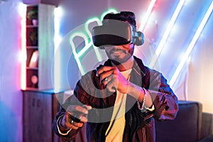 Young man on neon background playing video game virtual reality or VR headset at home using gamepads - concepts of