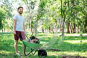 young man with new trees in wheelbarrow standing