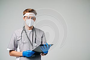 Young man nurse hospital worker in medical protective mask holding notepad isolated on white background with copy space