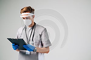 Young man nurse hospital worker in medical protective mask holding notepad isolated on white background with copy space