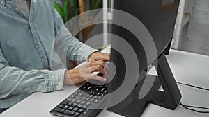 Young man in office typing on keyboard at a computer, displaying focus and productivity in a modern workplace environment with