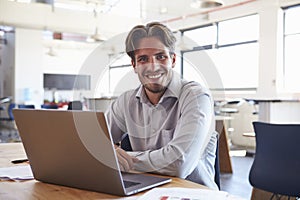 Young man in office using laptop computer smiling to camera