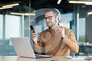 A young man, an office worker, a freelancer works in the office with a laptop and listens to music in headphones, rests