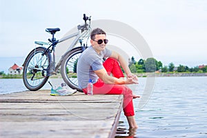 Young man, one happy tourist bicyclist map wearing in gray shirt with glasses sitting at the beach and resting after bicycle ride