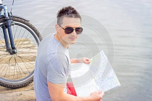 Young man, one happy tourist bicyclist with route map wearing in gray shirt with glasses