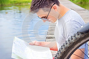 Young man, one happy tourist bicyclist with route map wearing in gray shirt with glasses