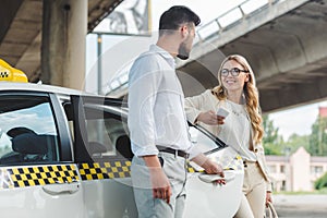 young man opening door of taxi and looking at smiling blonde woman