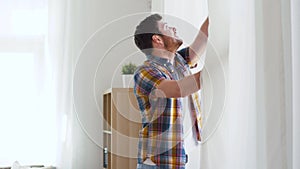 Young man opening window curtain at home