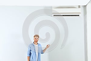 Young man operating air conditioner with  control indoors. Space for text