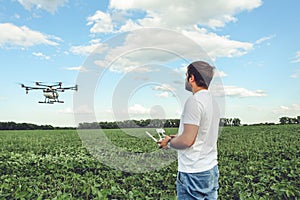 Young man operating of flying drone octocopter at the green field.