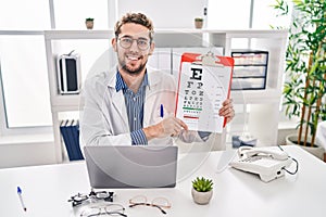 Young man optician holding snellen test at clinic