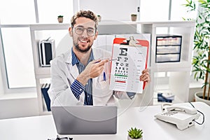 Young man optician holding snellen test at clinic