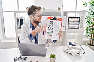 Young man optician holding snellen test at clinic